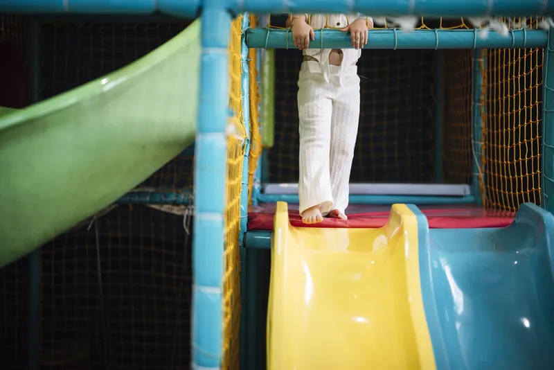 Indoor parky a trampolínová centra: dítě na vrcholu barevné skluzavky v kryté herně