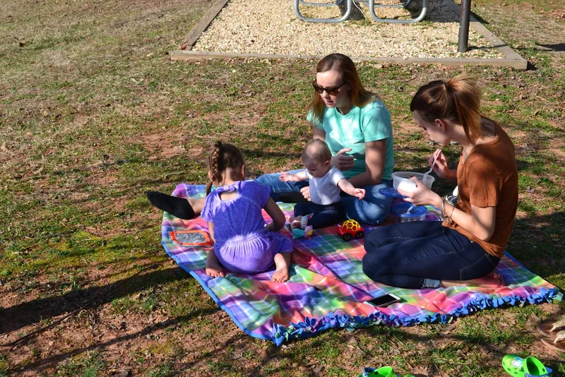 Piknik s dětmi: rodina s miminkem a holčičkou na barevné dece v parku