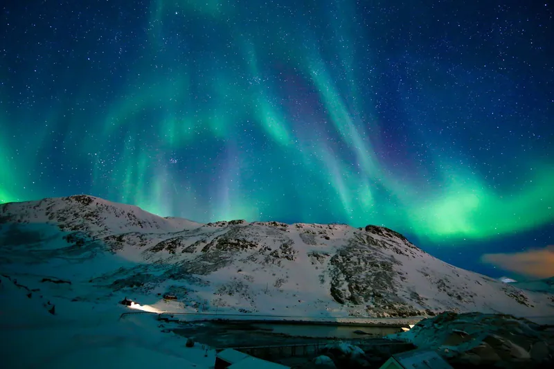 Green northern lights over snowy mountains in northern Norway, a highlight of winter adventures with kids