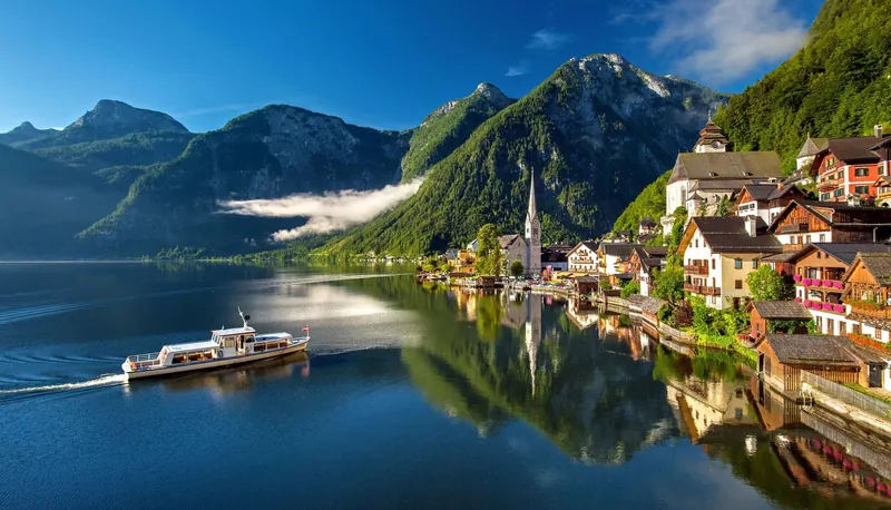 Boat on Lake Hallstatt below green mountains, a postcard view of an Alpine summer with kids