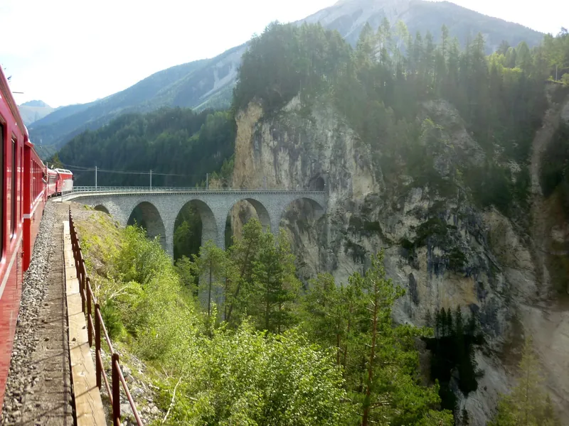 Red Rhaetian Railway train approaching the Landwasser Viaduct in summer, a highlight of Interrail with kids