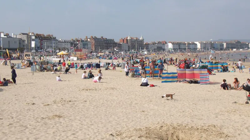 Families with windbreaks on a busy sandy beach in Weymouth, a classic UK staycation for the summer holidays