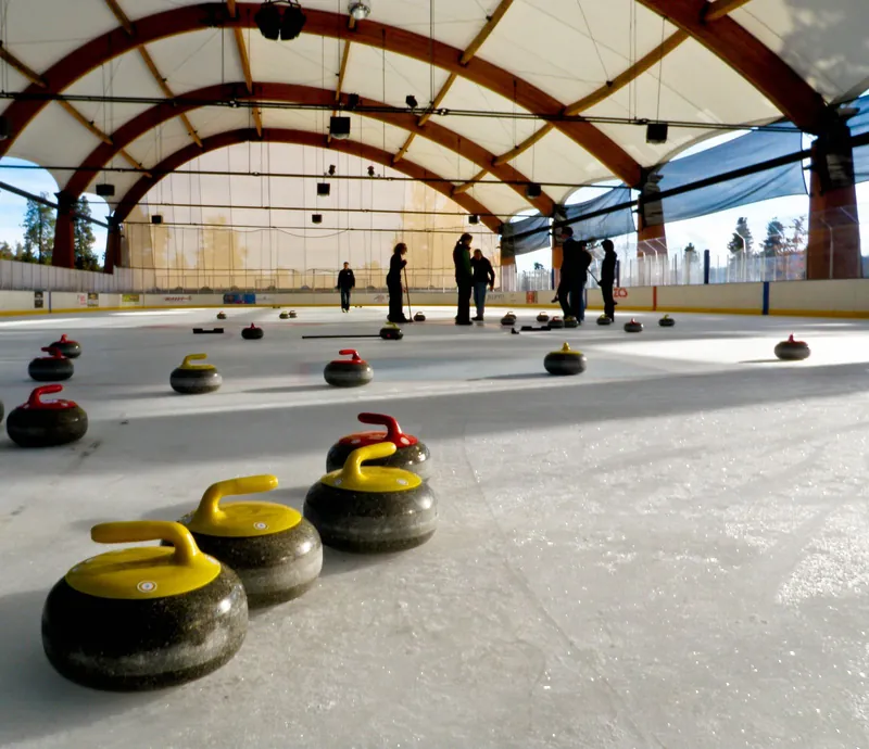 Curling stones lined up on the ice of a covered rink, a fun way to try winter sports with kids