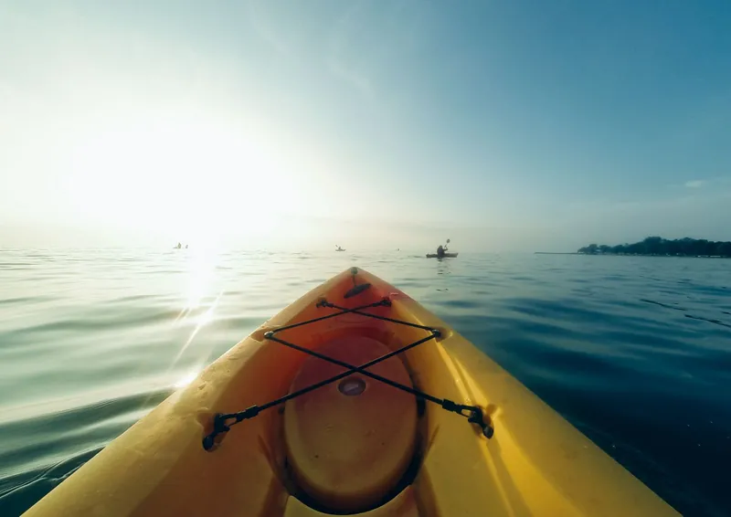 Bow of a yellow kayak on a calm lake with paddlers ahead, the kind of Father's Day adventures kids remember