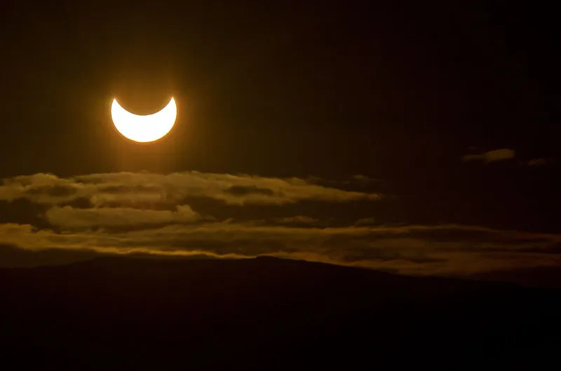 Crescent sun during a partial eclipse low over hills and clouds, what families can expect watching a solar eclipse with kids